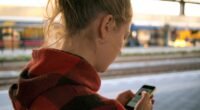 Mulher de costas olhando a tela do celular em uma plataforma de estação