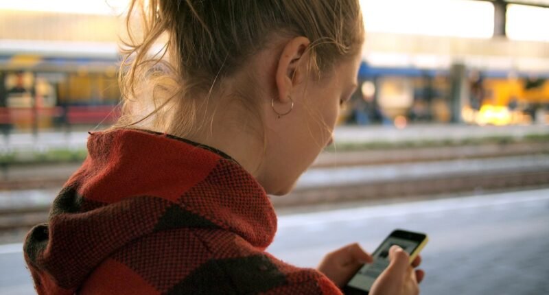 Mulher de costas olhando a tela do celular em uma plataforma de estação