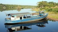 Barco de madeira azul ancorado em um rio calmo da Amazônia, com mata na margem