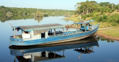 Barco de madeira azul ancorado em um rio calmo da Amazônia, com mata na margem