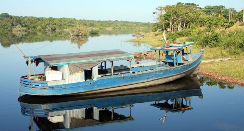 Barco de madeira azul ancorado em um rio calmo da Amazônia, com mata na margem