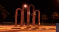 Arcos da Orla de Atalaia iluminados à noite, em Aracaju, com coqueiros ao fundo