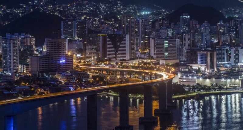 Vista noturna da Terceira Ponte iluminada, ligando Vitória a Vila Velha, com prédios ao fundo
