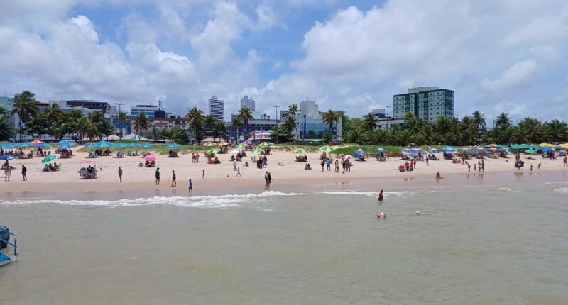 Praia de Tambaú, em João Pessoa, com banhistas na areia e prédios baixos na orla