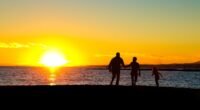 Silhuetas de um homem, uma mulher e uma criança pequena em contraluz, ao pôr do sol