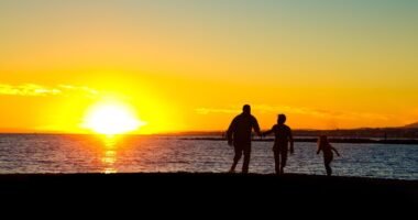 Silhuetas de um homem, uma mulher e uma criança pequena em contraluz, ao pôr do sol