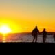 Silhuetas de um homem, uma mulher e uma criança pequena em contraluz, ao pôr do sol